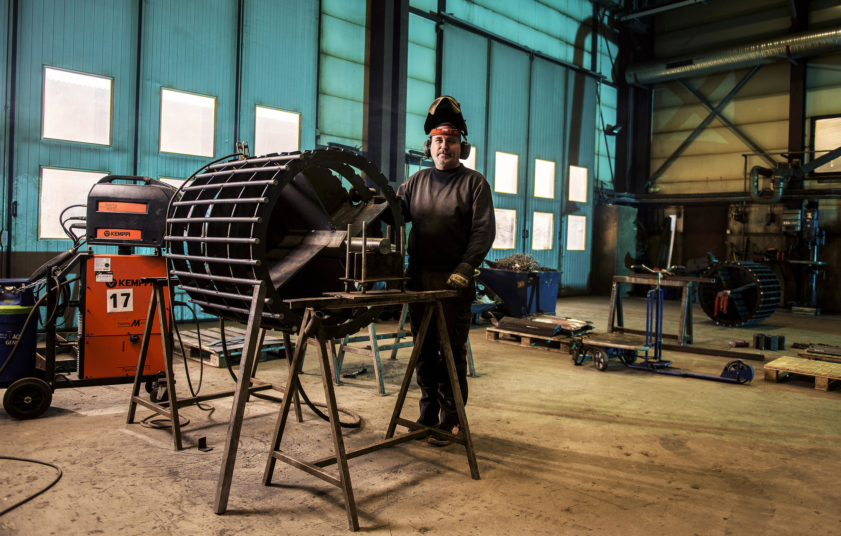 Ansatt i TI Industrier i sveiseutstyr ser opp fra arbeidet og smiler.